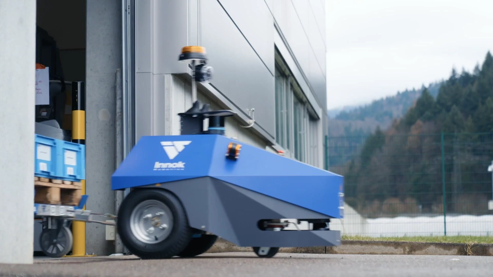 Autonomiczny AGV INDUROS holuje wózek przez bramę hali na plac